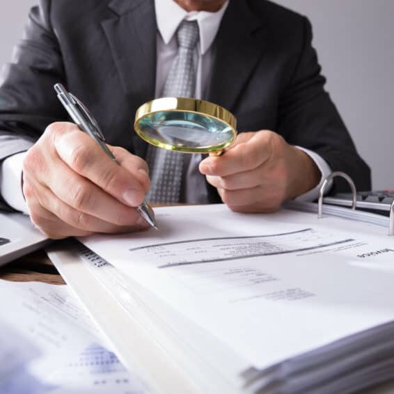 Person writing on paper holding a magnifying glass in the other hand.